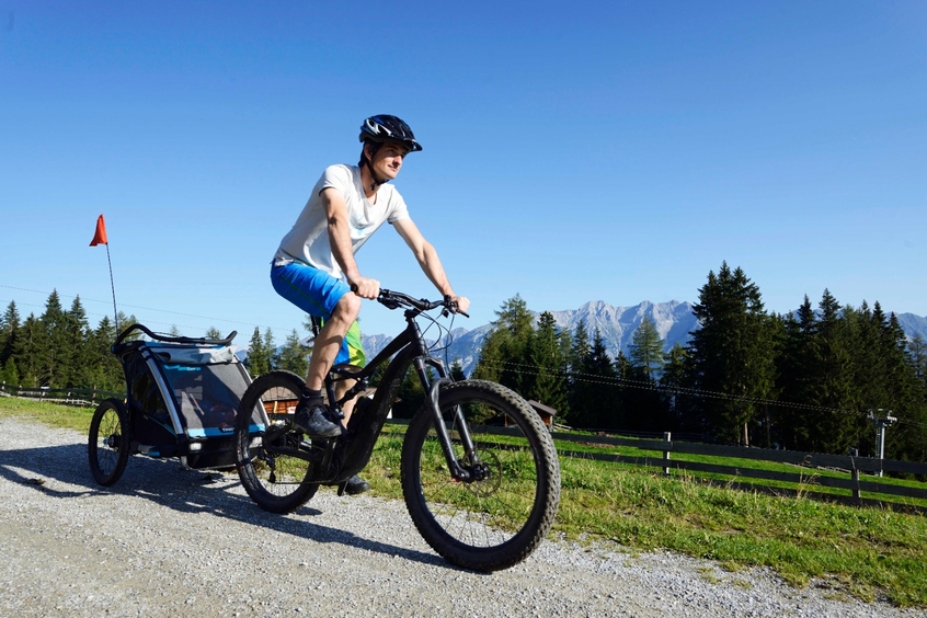 Mann mit E-Bike, der Anhänger mit Kind zieht. 