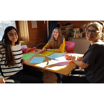 Drei Mädchen sitzen an Tisch und gestalten Plakate