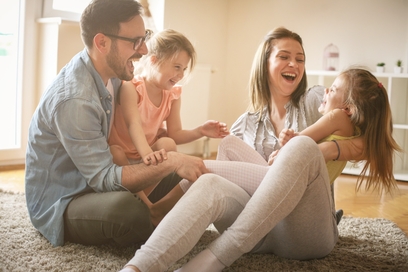 Junge Familie mit 2 kleinen Töchtern auf Fußboden sitzend und lachend.